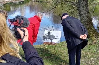 Een cameravrouw filmt twee mensen die bij een afbeelding bij de vijver in het park staan te kijken